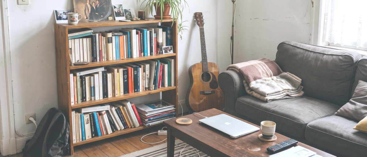 Coin de séjour loué : étagère de livres, ordinateur portable et guitare appuyée contre le mur.