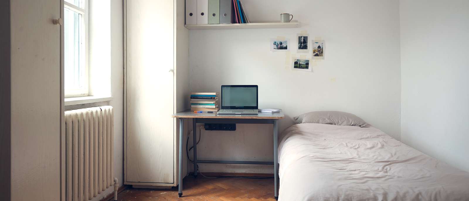 Chambre d'étudiant meublée, bureau sous la fenêtre, étagère et lit simple, fin d'après-midi.