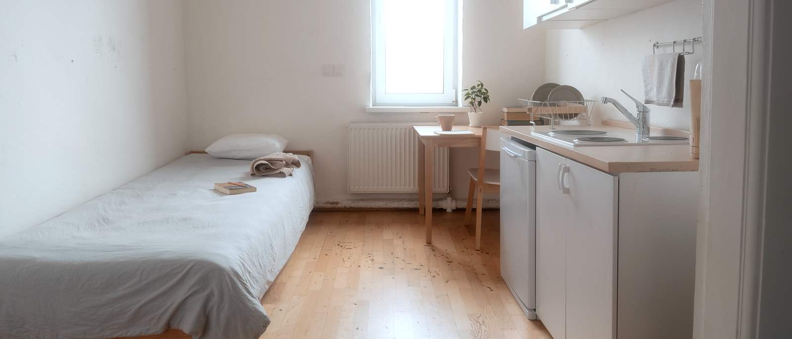 Studio d’une pièce, lit simple, kitchenette et parquet clair.